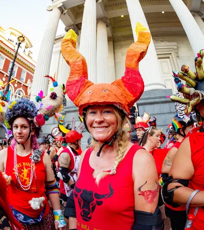 Group of people in red shirts and elaborate horned helmets gathered outside a historic building with columns.