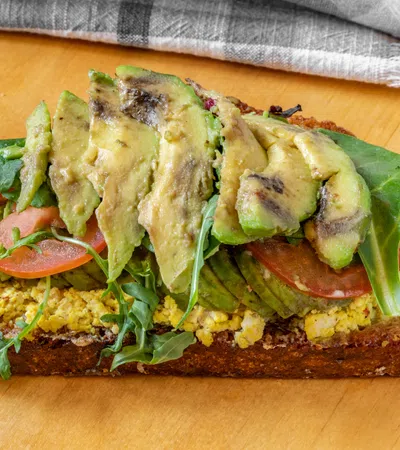 Delicious open-faced sandwich with avocado, tofu, tomatoes, and greens on rustic bread.