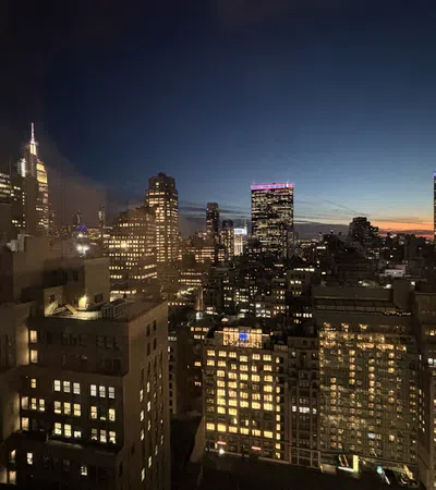 City skyline at dusk with illuminated skyscrapers and a clear fading sunset in the background.