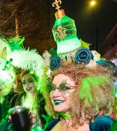 Two women in elaborate, glowing green Mardi Gras costumes with feathers and decorative headpieces at night