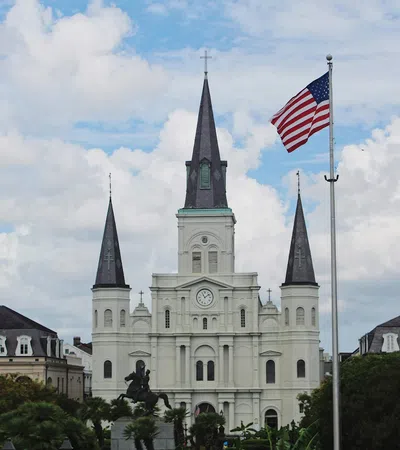 St. Louis Cathedral with three spires and American flag against partly cloudy sky in New Orleans.