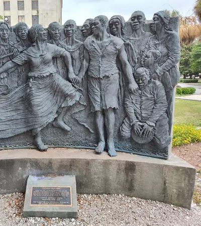 Bronze relief sculpture of joyful people dancing and playing drums in an outdoor park setting.