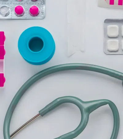 Medical supplies including stethoscope, pill organizer, bandages, tablets, and medical tape on a white surface.