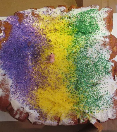 Traditional King Cake with purple, yellow, and green sugar, white icing, and a tiny plastic baby in the center.