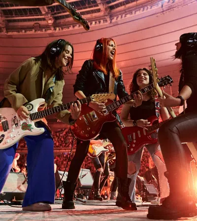 Energetic band performing live on stage with guitars and vibrant crowd in a large stadium concert.