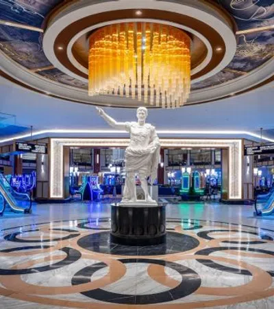 Modern casino lobby with marble floor, central statue, large chandelier, and blue escalators on both sides