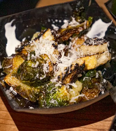 Roasted Brussels sprouts topped with grated cheese served in a black bowl on a wooden table