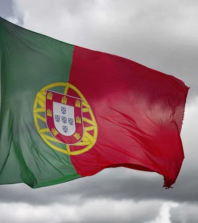 Portuguese national flag waving on a pole against a cloudy sky background