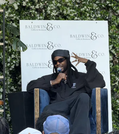 Man in black clothing and sunglasses speaking into microphone at Baldwin & Co. Coffee & Bookstore event.