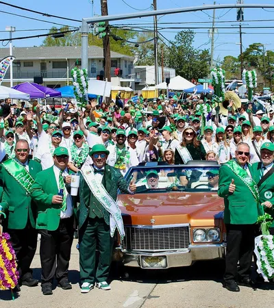 Group dressed in green suits and hats posing in front of a classic car during a festive St. Patrick's Day parade.