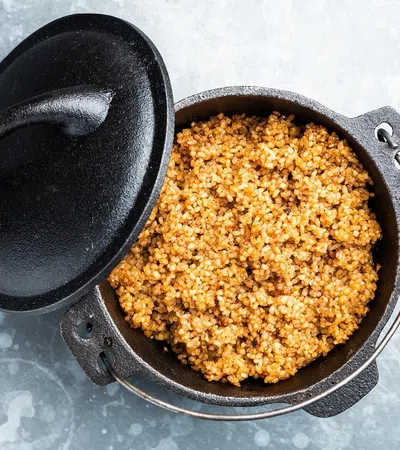 Cast iron pot with cooked seasoned bulgur wheat on a light textured surface with lid ajar