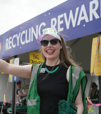 Woman in a green vest at a recycling event, promoting recycling rewards with enthusiasm.
