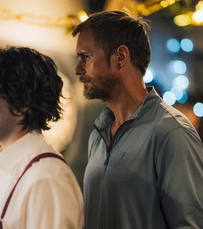 Two men standing side by side indoors with blurred lights and people in background