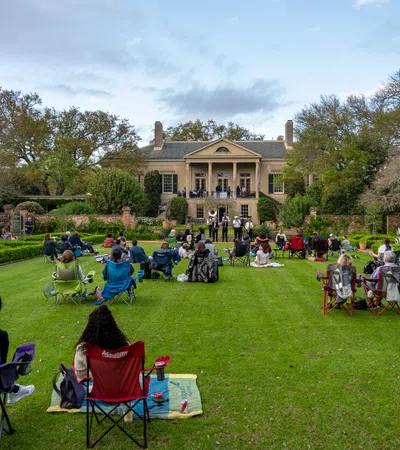 a group of people sitting in chairs in a grassy area with a building in the background