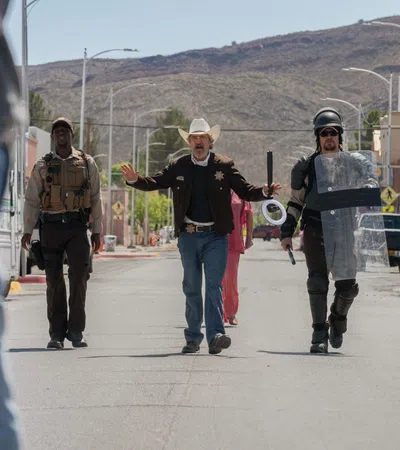 Sheriff and law enforcement officers walking down a sunny street in a desert town with mountains in background