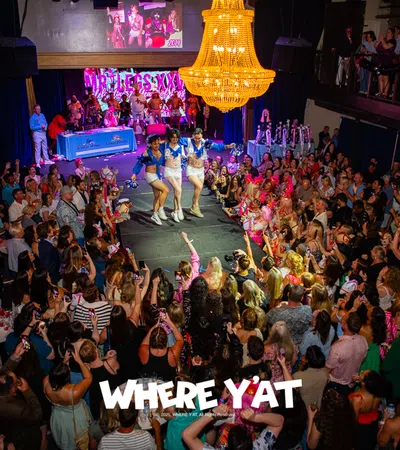 Crowded event with performers dancing on stage under a large chandelier in a vibrant venue packed with an enthusiastic audience.