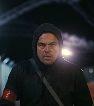 Man in dark hoodie with red armband walking at night in an urban area under bright streetlights.