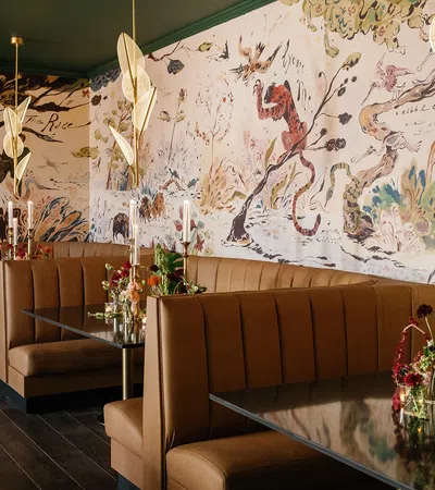 Cozy restaurant booths with floral arrangements and artistic mural on wall under modern gold pendant lights.
