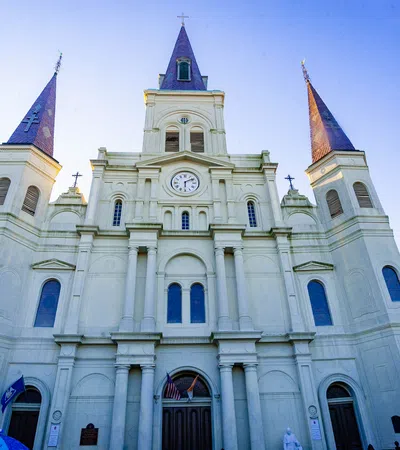 Front view of St. Louis Cathedral with three spires and clock, under clear blue sky at sunset.