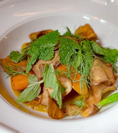 A gourmet dish with crispy vegetables and fresh herbs served in a white bowl.