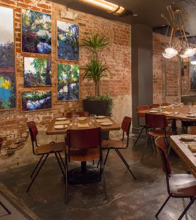Cozy restaurant interior with wooden tables, colorful abstract art on brick walls, and modern lighting fixtures.