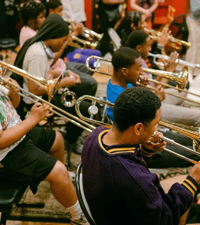 Young musicians playing trombones in a group rehearsal inside a music studio with wooden floors.