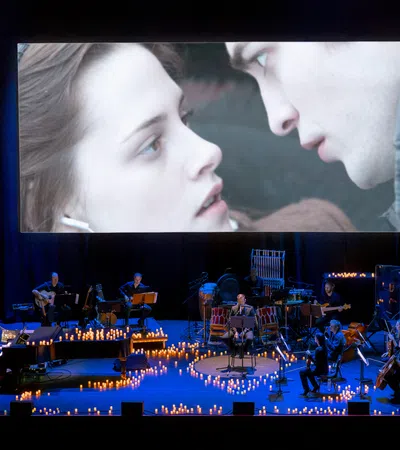 A live performance featuring musicians and a large screen displaying a romantic scene.