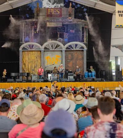 A lively music performance on stage at a festival, with a large audience enjoying the show.