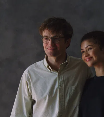 Smiling man with glasses and woman posing together against a dark gray textured background.