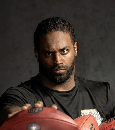 Serious male football player holding three footballs wearing a black shirt against a dark background