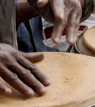 Close-up of hands playing traditional drums with textured beige drumheads in a lively setting