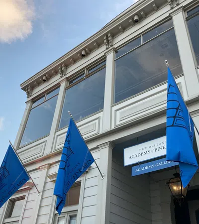 Exterior view of New Orleans Academy of Fine Arts with blue flags and clear sky at dusk