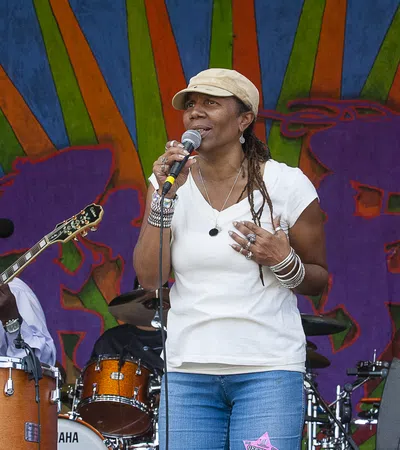 Female vocalist singing on stage with band members playing guitar and drums against vibrant backdrop