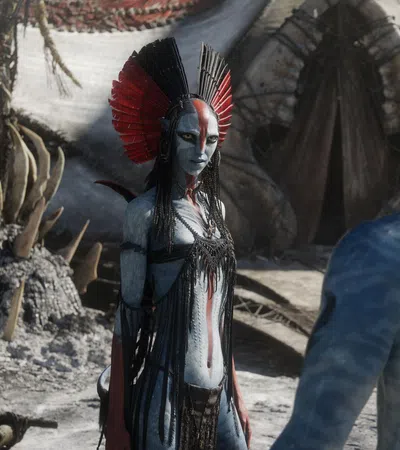 Two blue-skinned Na'vi characters in elaborate costumes face each other in a tribal village setting from Avatar.