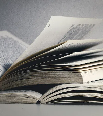Open books with pages flipping, showing printed text on a neutral background in soft lighting.