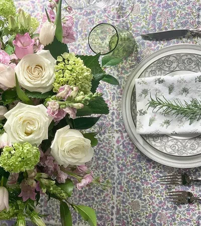 Elegant floral centerpiece with white roses and green hydrangeas beside a lavender-themed place setting with a rosemary napkin.