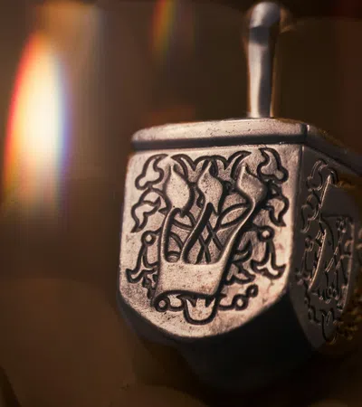 Close-up of a silver decorative dreidel with intricate Hebrew engravings and soft warm lighting.