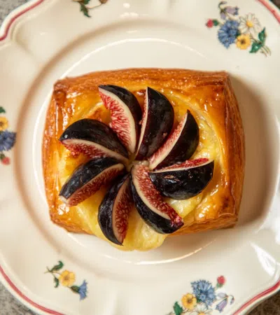 Fresh fig slices arranged on a custard-filled puff pastry on a floral vintage plate.