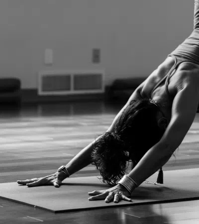 Woman practicing yoga in downward dog pose on a mat in a spacious studio with wooden floor.