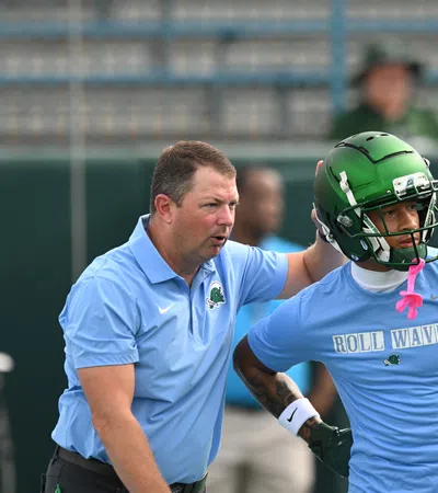 Football coach instructing player wearing green helmet and blue Roll Wave shirt during practice session