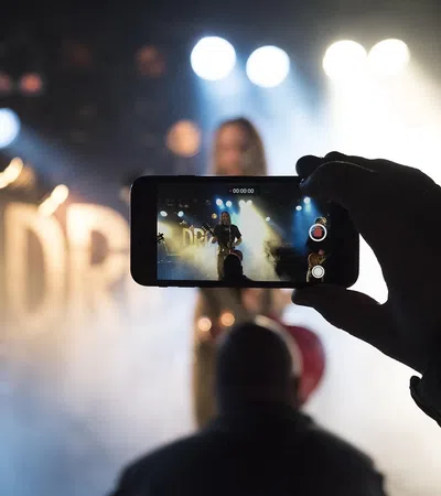 Person recording a live music performance on smartphone with stage lights and smoke effects in background