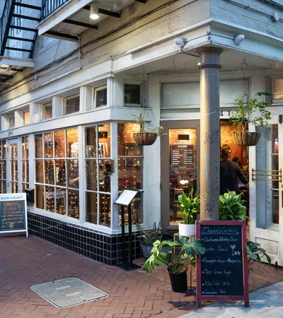 Cozy cafe exterior with large windows, hanging plants, chalkboard menu, and warm indoor lighting at dusk