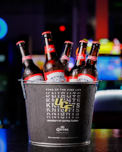 Metal bucket with University of Central Florida logo holding five chilled Budweiser beer bottles on a bar counter.