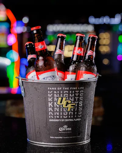 Bucket of Corona beers branded with University of Central Florida Knights logo and neon lights in background