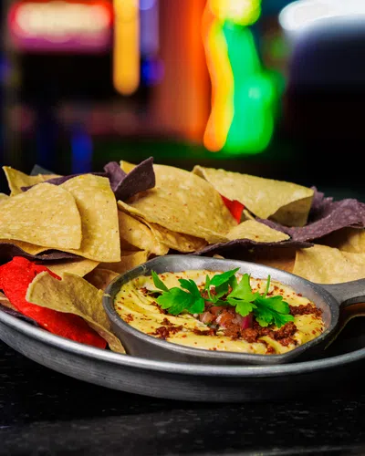 Plate of colorful tortilla chips served with creamy hummus dip garnished with parsley on a dark surface.