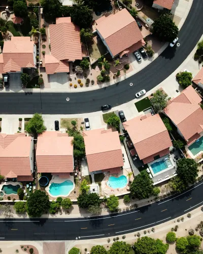 Aerial view of suburban neighborhood with houses, swimming pools, driveways, and curved roads.
