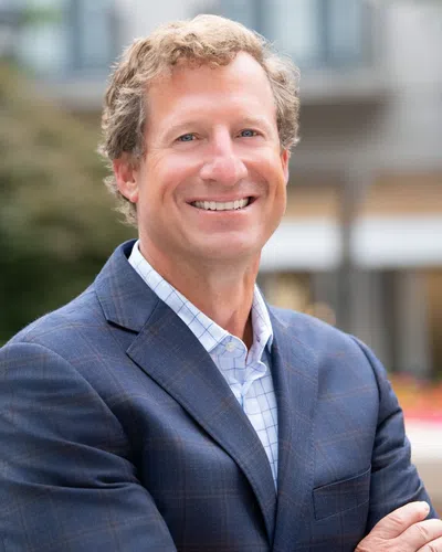 Smiling man in blue checkered suit with arms crossed outdoors in an urban setting
