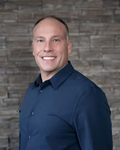Smiling bald man in a dark blue dress shirt posed in front of a stone wall background