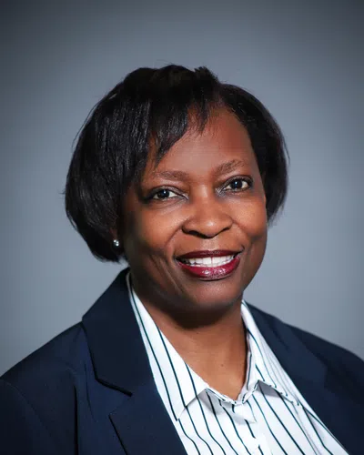 Professional smiling Black woman in a navy blazer and striped white shirt against a plain background