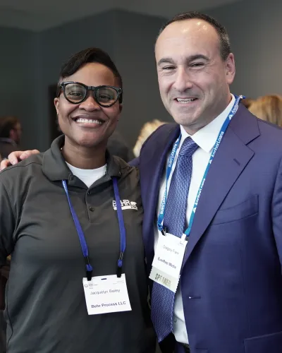 Smiling professionals at a networking event wearing name badges and business attire, engaging and posing for photo.